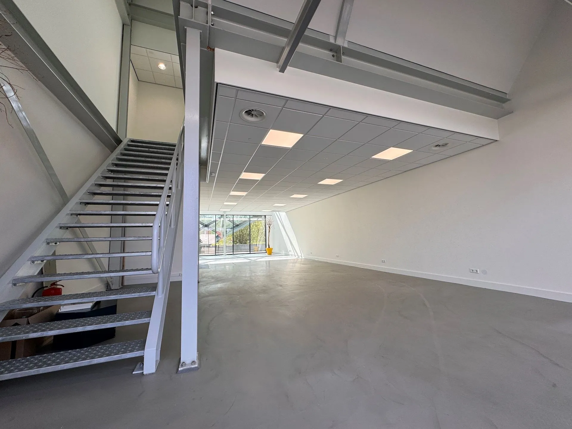 Lege, moderne kantoorruimte in Mart Stamhof met een metalen trap en grote ramen aan de voorzijde.